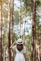 mulher viajante feliz em pé e olhando floresta de pinheiros, turista solo em vestido branco e chapéu viajando em pang oung, mae hong son, tailândia. conceito de viagens, viagens e férias foto