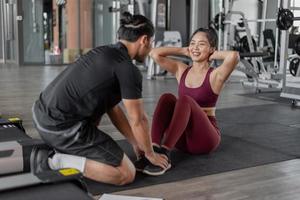 exercícios de mulher asiática com personal trainer no ginásio. mulher saudável asiática fazendo exercícios abdominais em fitness com treinador pessoal. foto