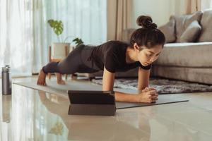 mulher asiática fazendo prancha de ioga e assistindo aula de ioga online. jovem se exercitando em casa. foto