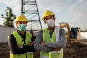 homens de engenheiros trabalhando no canteiro de obras. homens trabalhadores asiáticos usando máscara facial e braços cruzados no canteiro de obras. foto