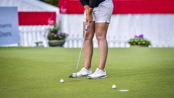 golfista empurrando a bola de golfe branca para o buraco no campo de golfe no jogo de competição de golfe, raios de luz solar e fundo desfocado