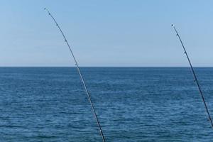 duas varas de pesca contra o oceano azul ou fundo do mar, copie o espaço. esperando a maior carga. esporte de relaxamento meditativo. foto