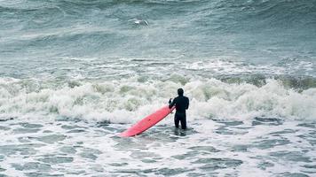 surfista masculino em traje de banho nas ondas do mar com prancha vermelha foto