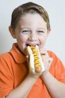 jovem garoto segurando comendo cachorro-quente