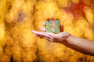 feliz Natal e Feliz Ano Novo. caixa de presente nas mãos da mulher com bokeh brilhante. foto