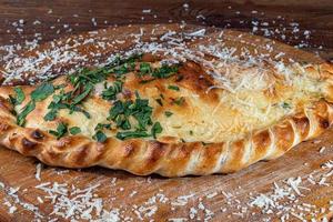 calzone de pizza com bacon e queijo, ervas e tomate cereja. com mussarela, camarões e polvos, mexilhões e outros produtos em um fundo de madeira. foto