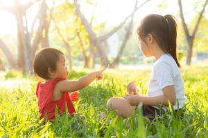 linda criança asiática sentada jogando no verão no parque com diversão e alegre na grama verde, atividade de crianças com relaxamento e felicidade juntos no conceito de prado, família e férias. foto