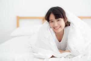 belo retrato jovem mulher asiática mentindo e sorria enquanto acorda com o nascer do sol de manhã, menina com feliz e divertido no quarto, estilo de vida e conceito de relaxamento. foto