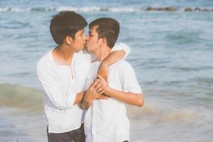 retrato homossexual jovem casal asiático em pé abraço e beijo na boca juntos na praia no verão, ásia gay indo turismo para lazer com romântico e felicidade em férias no mar, conceito legal lgbt. foto