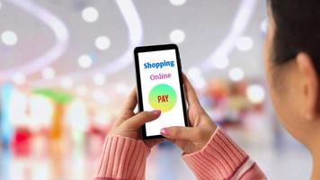foco seletivo na mão feminina jovem no suéter de malha rosa usando aplicativo no smartphone para compras de pagamento on-line com fundo de shopping desfocado foto