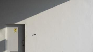 luz solar e sombra na superfície da parede cinza e porta da sala de controle elétrico com sinal de aviso amarelo em estilo minimalista, conceito de arquitetura exterior foto