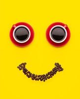 xícara de café e grãos de café com conceito de rosto de sorriso, vista superior sobre fundo amarelo. para o conceito feliz de manhã foto