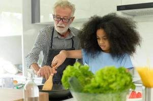 atividades de férias em família com avô e netos. cozinhar o jantar juntos para o avô da família está ensinando a cozinhar para sua neta meia-asiática afro-americana