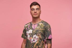 retrato interior de atraente jovem de cabelos curtos em camiseta casual posando sobre fundo rosa, olhando calmamente para a câmera com aparência confiante foto