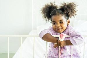 menina fofa afro-americana segurando tomando sorvete na cama no quarto foto