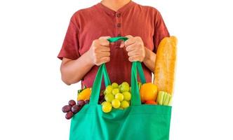 homem segura sacola de compras reutilizável verde ecologicamente correta cheia de produtos de mercearia frescos completos de frutas e legumes isolados no fundo branco com traçado de recorte foto