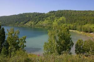 lago pitoresco cercado por montanhas com grama verde e árvores. foto