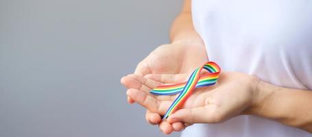 mão segurando a fita de arco-íris lgbtq para apoio à comunidade lésbica, gay, bissexual, transgênero e queer e conceito de mês do orgulho foto