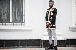 mega homem africano elegante em pose de jaqueta tradicional. elegante negro de chapéu e óculos de sol com charuto na mão. foto