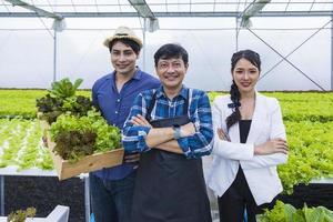 agricultores locais asiáticos cultivando sua própria alface de salada de carvalho verde na estufa usando sistema de água hidropônica em abordagem orgânica para negócios próprios da família foto