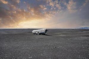 vista do naufrágio do avião danificado na praia de areia preta em solheimasandur no pôr do sol foto