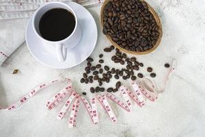 xícara de café e fundo de grãos de café com torneira de medida na mesa branca. foto