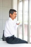 velho de negócios asiáticos com camisa branca trabalhando e tomando café na sala de reuniões no escritório foto