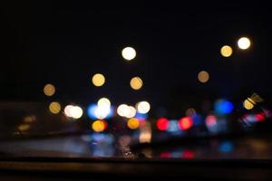 de um pára-brisa de carro com limpadores de pára-brisa em ação. luzes embaçadas lá fora na noite foto