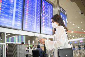 uma mulher viajante está usando máscara protetora no aeroporto internacional, viaja sob pandemia covid-19, viagens de segurança, protocolo de distanciamento social, novo conceito de viagem normal. foto