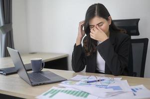 estressada jovem empresária trabalhando no laptop com documentos no escritório moderno, conceito de carga de trabalho foto