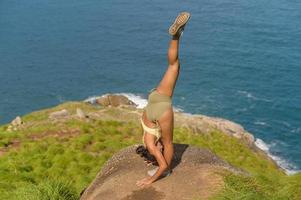 linda mulher asiática em roupas esportivas fazendo ioga no pico da montanha à beira-mar após o conceito de trekking, viagens e meditação. foto