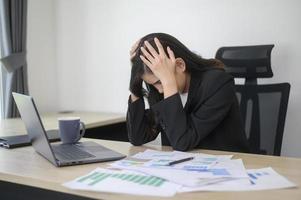 estressada jovem empresária trabalhando no laptop com documentos no escritório moderno, conceito de carga de trabalho foto