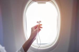 mão de mulher segurando fones de ouvido em aeronaves de janela foto