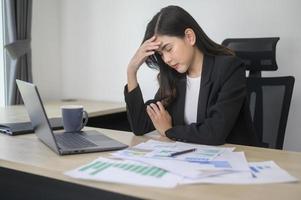 estressada jovem empresária trabalhando no laptop com documentos no escritório moderno, conceito de carga de trabalho foto