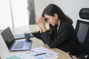 estressada jovem empresária trabalhando no laptop com documentos no escritório moderno, conceito de carga de trabalho foto