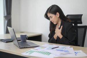 estressada jovem empresária trabalhando no laptop com documentos no escritório moderno, conceito de carga de trabalho foto