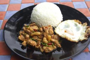 manjericão, frango, ovo frito, comida tailandesa o estilo da casa não é sofisticado em uma placa de cerâmica preta colocada em uma mesa de concreto xadrez. pronto para servir e entrega foto