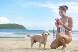 jovem mulher bonita de biquíni com seu cachorro curtindo e relaxando na praia, verão, férias, feriados, conceito de estilos de vida. foto