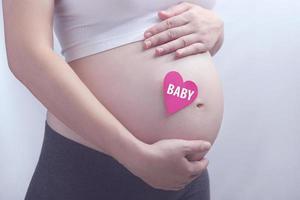 mulher grávida segurando seu feto com papel de coração, saudável para nova família foto