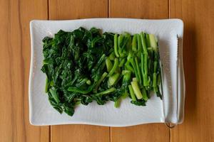 vegetal de couve tailandesa chinesa deslizada e cozida separada estava no retângulo branco sobre a mesa de madeira. foto