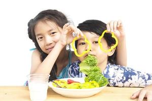 menino e menina asiáticos mostrando desfrutar de expressão com legumes coloridos frescos e copo de leite isolado sobre fundo branco foto