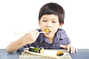 menino adorável asiático está comendo sushi isolado sobre fundo branco foto