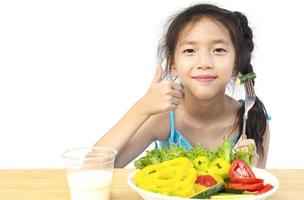 menina adorável asiática mostrando desfrutar de expressão com legumes coloridos frescos e copo de leite isolado sobre fundo branco foto