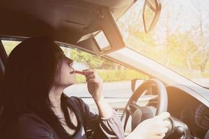 mulher maquiando o rosto usando batom enquanto dirige o carro, comportamento inseguro foto