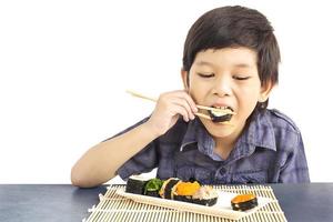 menino adorável asiático está comendo sushi isolado sobre fundo branco foto