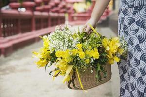 senhora asiática segurando cesta de flores amarelas frescas para participação na cerimônia budista tradicional local - pessoas com conceito de relacionamento religioso foto