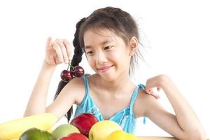 menina saudável asiática mostrando expressão feliz com variedade colorida de frutas e vegetais isolados sobre fundo branco foto