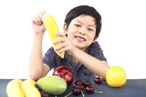 menino saudável asiático mostrando expressão feliz com variedade colorida de frutas e vegetais sobre fundo branco foto