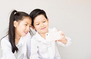 adorável casal asiático crianças da escola estão tirando selfie, 7 e 10 anos, sobre fundo cinza foto