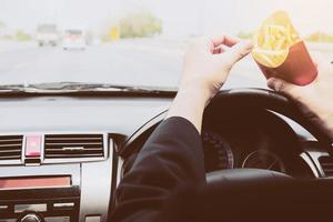 homem de negócios comendo batatas fritas e dirigindo o carro perigosamente foto